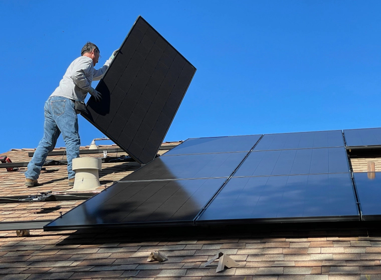 worker installing solar panels on the roofing of a house