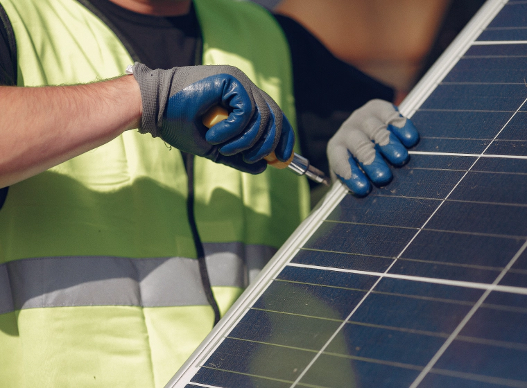 worker with a neon green vest with blue and grey gloves installing a solar panel
